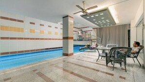 A swimming pool area with tiled walls, a ceiling fan, and lounge chairs.