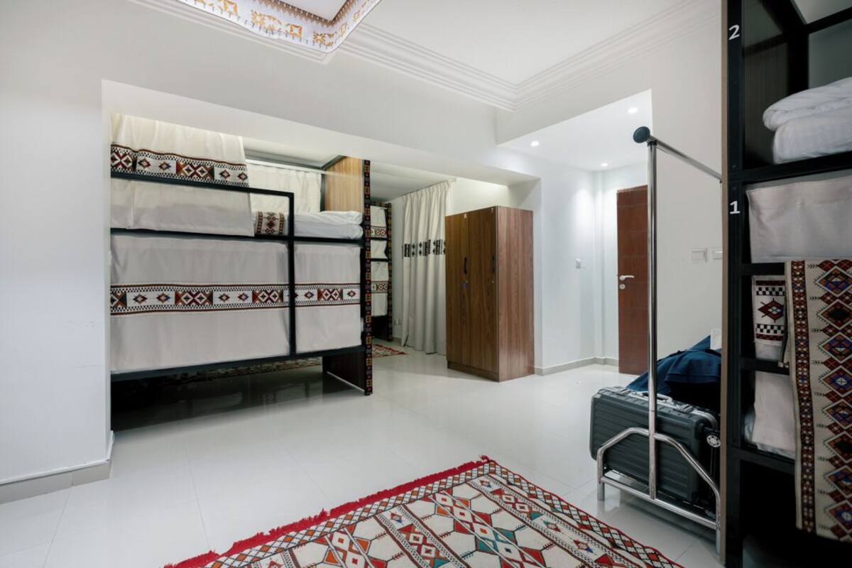Habitació d'hotel amb lliteres, un armari, una maleta i una catifa estampada.