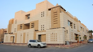 A multi-story building with a beige facade, featuring a white SUV parked in front.