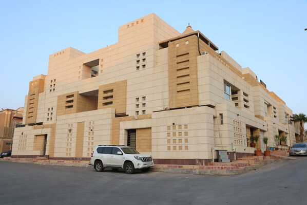 A multi-story building with a beige facade, featuring a white SUV parked in front. - Sands Inn Hostel (Riyadh)