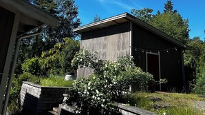A wooden building with a flat roof, surrounded by trees and a grassy area. - Cozy house with sea views, a spacious deck, and a beautiful garden (Stockholms län)