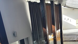 A modern room with a glass partition, wooden flooring, and a bed with a white cover. - Cozy house with sea views, a spacious deck, and a beautiful garden (Stockholms län)