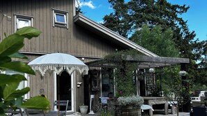 A wooden building with a covered patio area, outdoor seating, and potted plants. - Cozy house with sea views, a spacious deck, and a beautiful garden (Stockholms län)