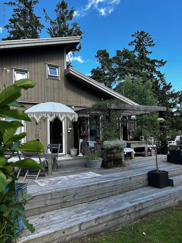 A wooden building with a covered patio area, outdoor seating, and potted plants.