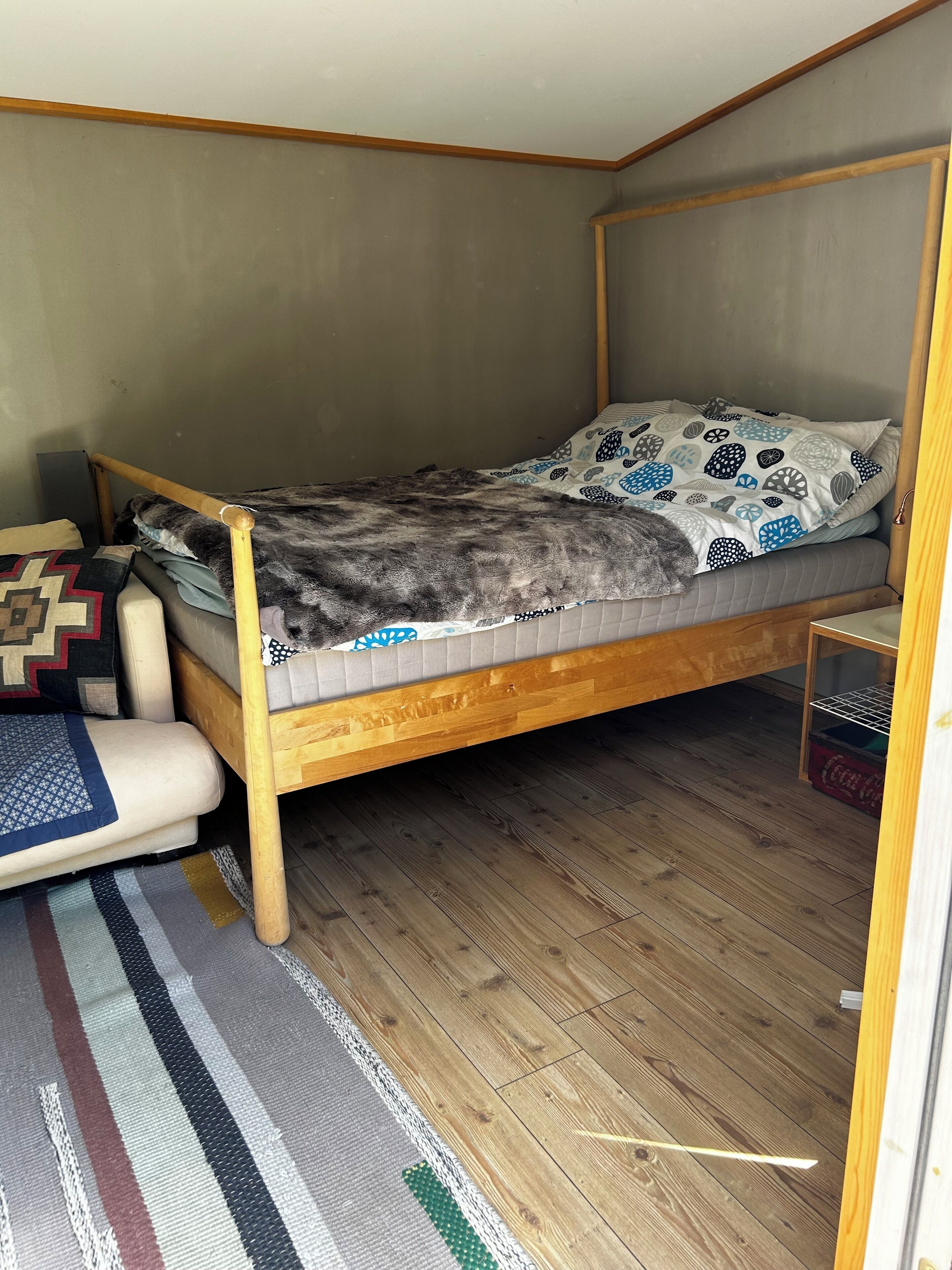 Una habitación pequeña con una cama individual, estructura de madera, colcha estampada y alfombra a rayas.