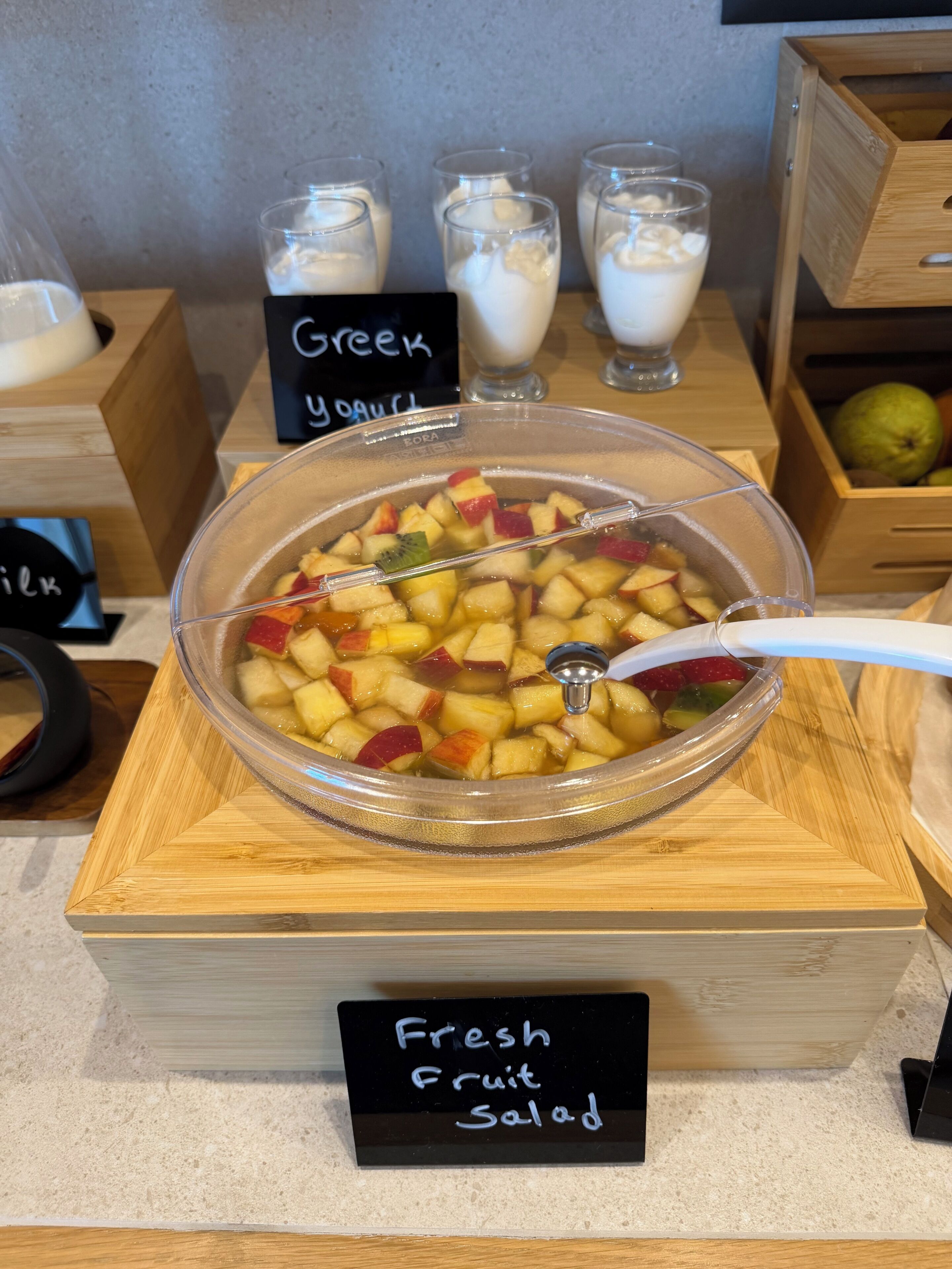A bowl of fresh fruit salad on a wooden stand with a sign labeled 'Fresh Fruit Salad'.