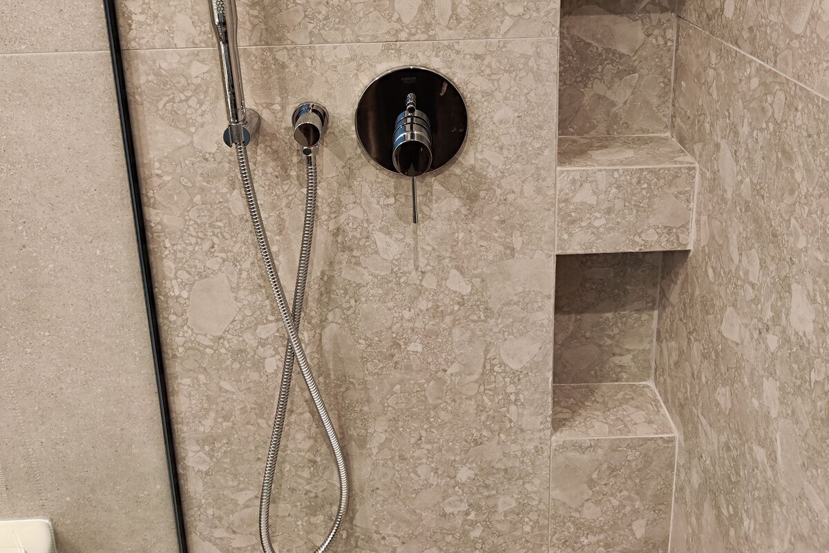 A bathroom with a shower, a sink, and a marble wall.