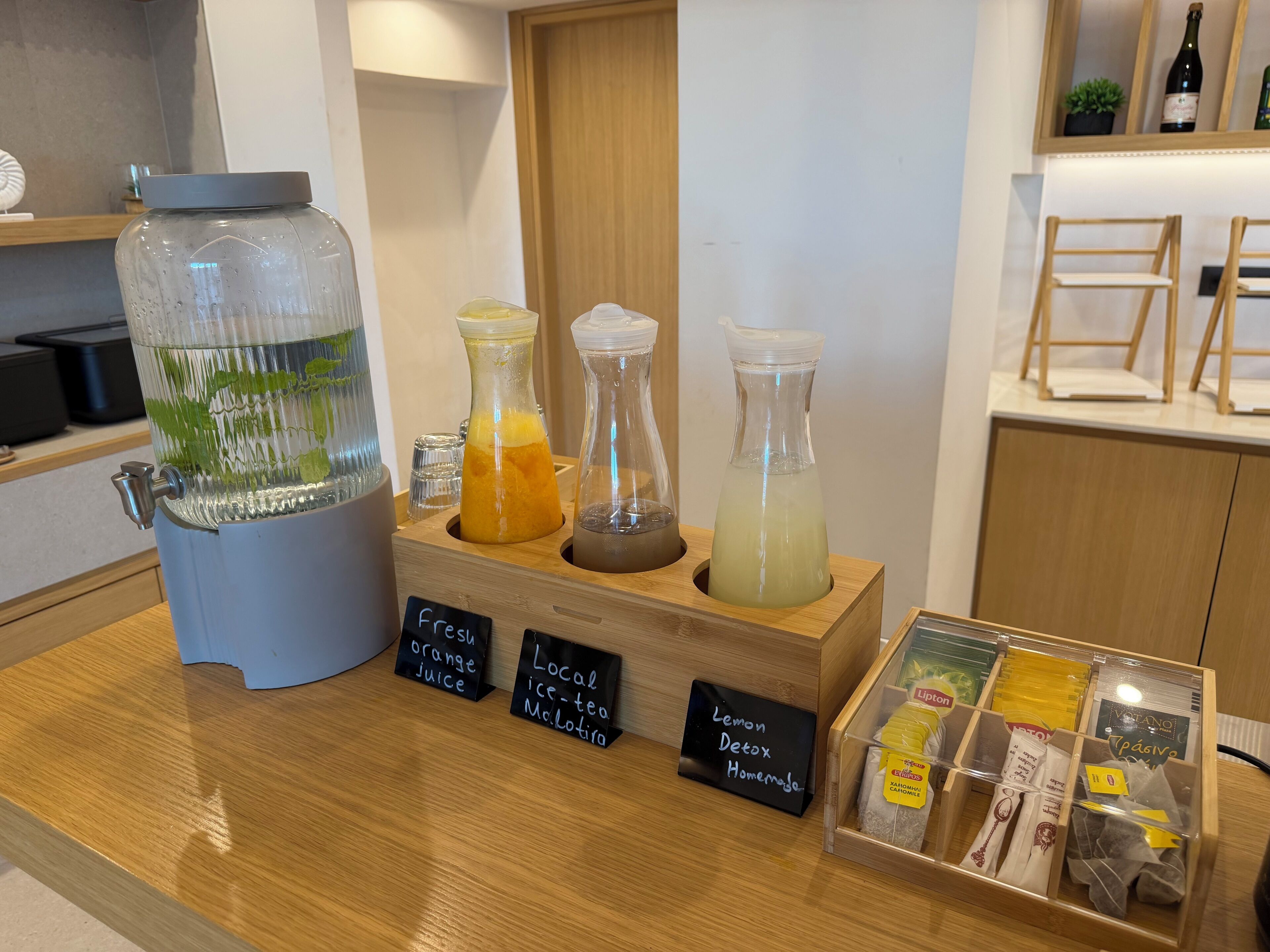 A counter with a water dispenser, three glass bottles with different colored liquids, and a box of tea bags.