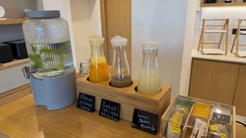 A counter with a water dispenser, three glass bottles with different colored liquids, and a box of tea bags.