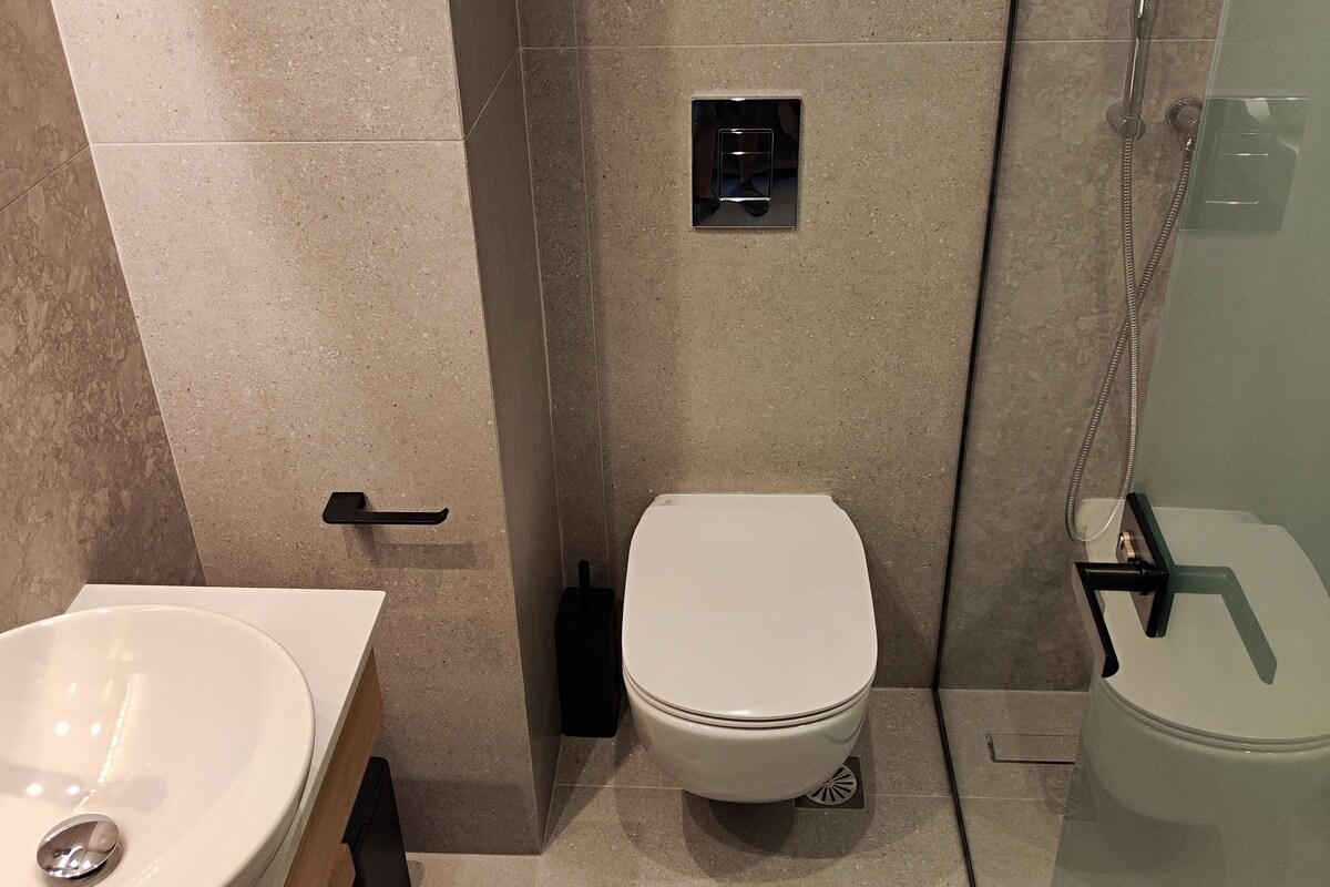 Un baño moderno con inodoro blanco, ducha con mampara de vidrio y lavamanos con espejo.