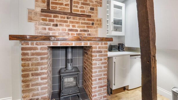 A kitchen with a brick fireplace, white cabinets, and a wooden beam ceiling.