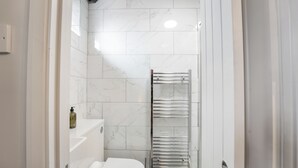 A modern bathroom with white marble tiles, a white toilet, a towel rack, and a green mat.