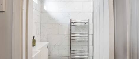 A modern bathroom with white marble tiles, a white toilet, a towel rack, and a green mat.