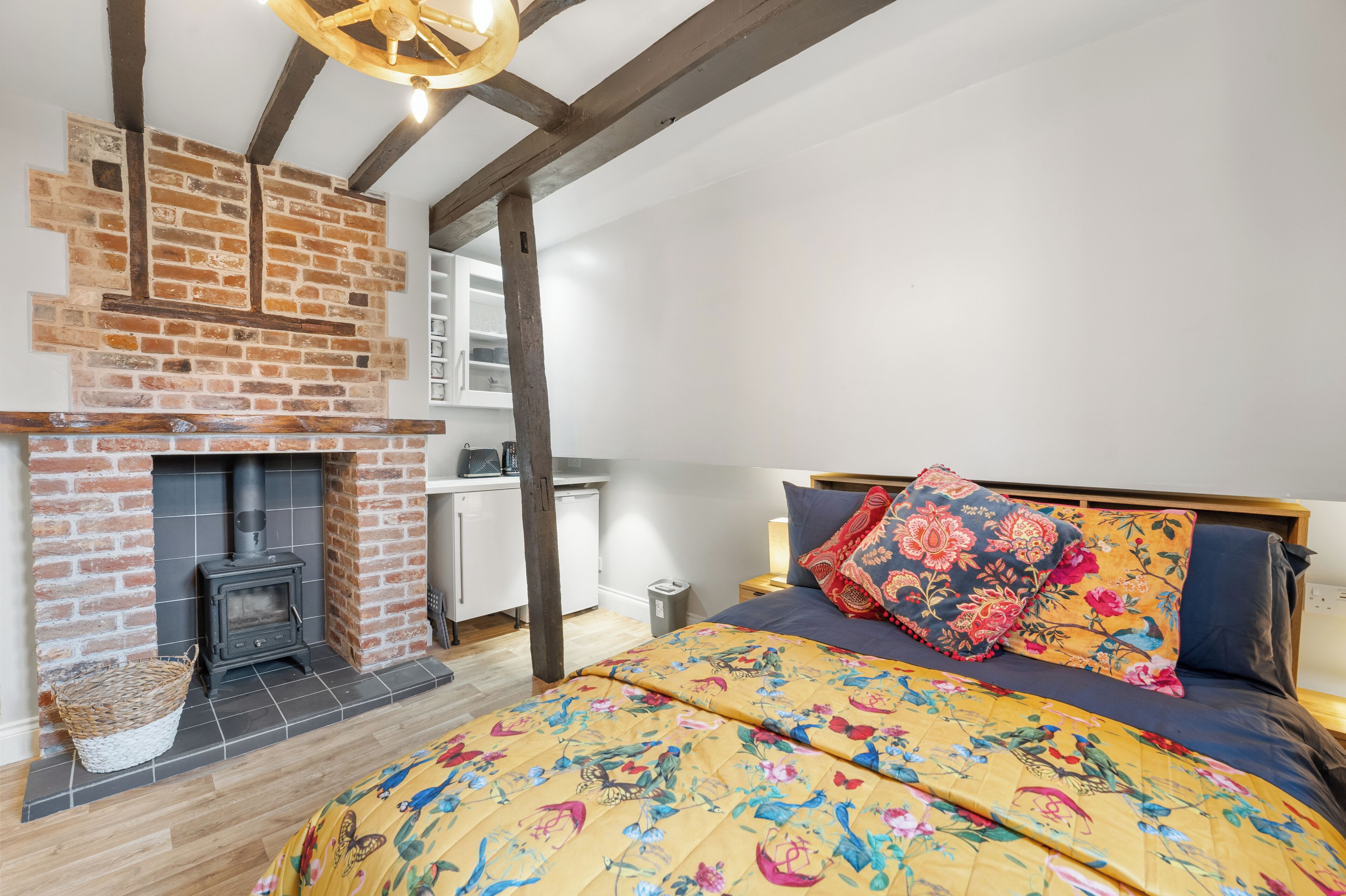 Un dormitorio con chimenea de ladrillo, una cama con ropa de cama floral y vigas de madera a la vista.