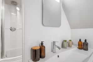 A modern bathroom with a glass shower enclosure, a white sink with two soap dispensers, a mirror, and a small potted plant. - 3 Bedroom City Centre Apartment (Canterbury)