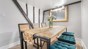 Een eetruimte met een houten tafel, stoelen en een bank. Op de tafel staat een vaas met bloemen, en aan de muur een spiegel.