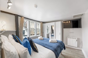 A bedroom with a large bed, a TV mounted on the wall, a window with curtains, and a radiator. - 3 Bedroom City Centre Apartment (Canterbury)