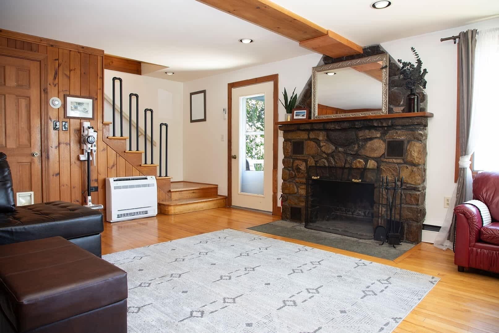 A living room with a stone fireplace, wooden staircase, and a red leather sofa.