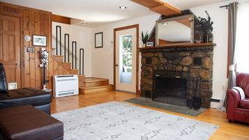 A living room with a stone fireplace, wooden staircase, and a red leather sofa.
