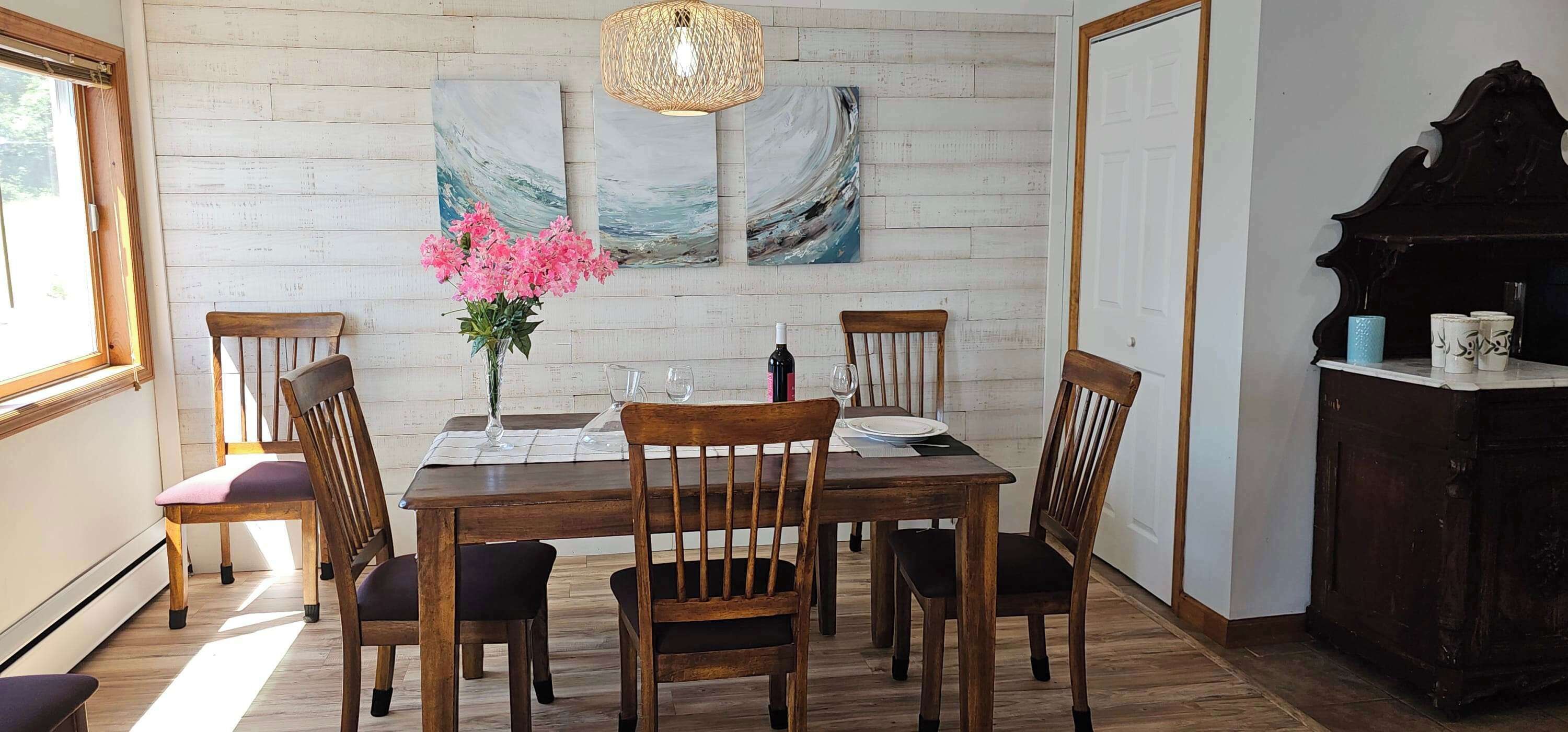 Un coin repas avec une table en bois, des chaises, un vase de fleurs et des œuvres d’art accrochées au mur.