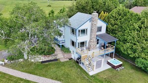 A two-story house with a stone chimney, a covered porch with outdoor furniture, and a hot tub. - ZaLo Manor Unit Lakefront hot tub, pets (Peru)