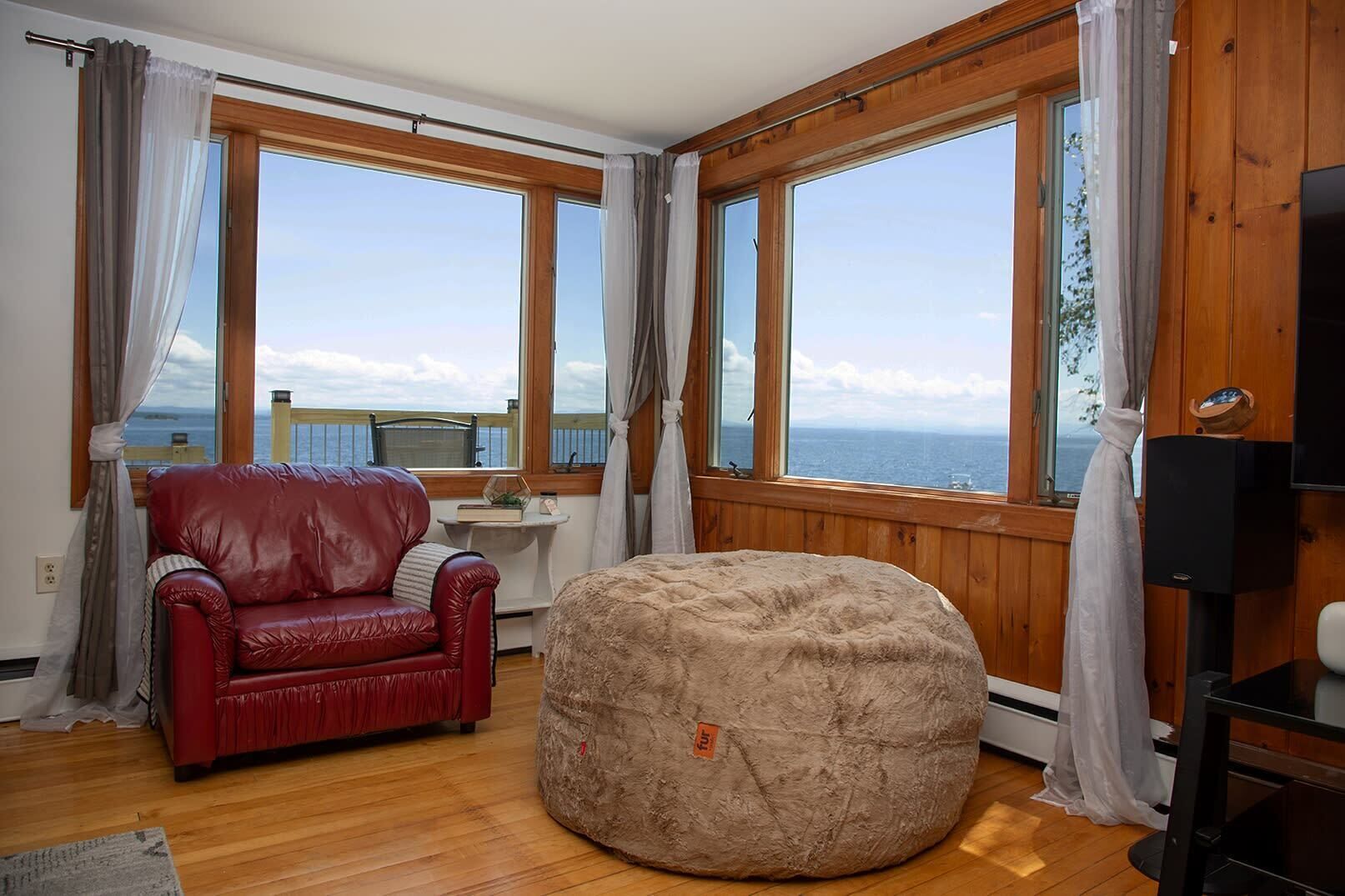 A room with a red leather sofa, a round bean bag, and large windows offering a view of the sea.
