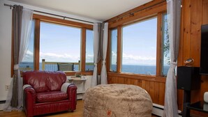 A room with a red leather sofa, a round bean bag, and large windows offering a view of the sea. - ZaLo Manor Unit Lakefront hot tub, pets (Peru)
