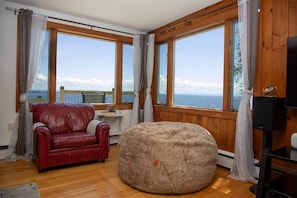 A room with a red leather sofa, a round bean bag, and large windows offering a view of the sea. - ZaLo Manor Unit Lakefront hot tub, pets (Peru)