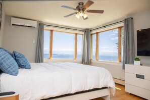 Ein Schlafzimmer mit Bett, Deckenventilator, Klimaanlage, Fernseher und Meerblick.