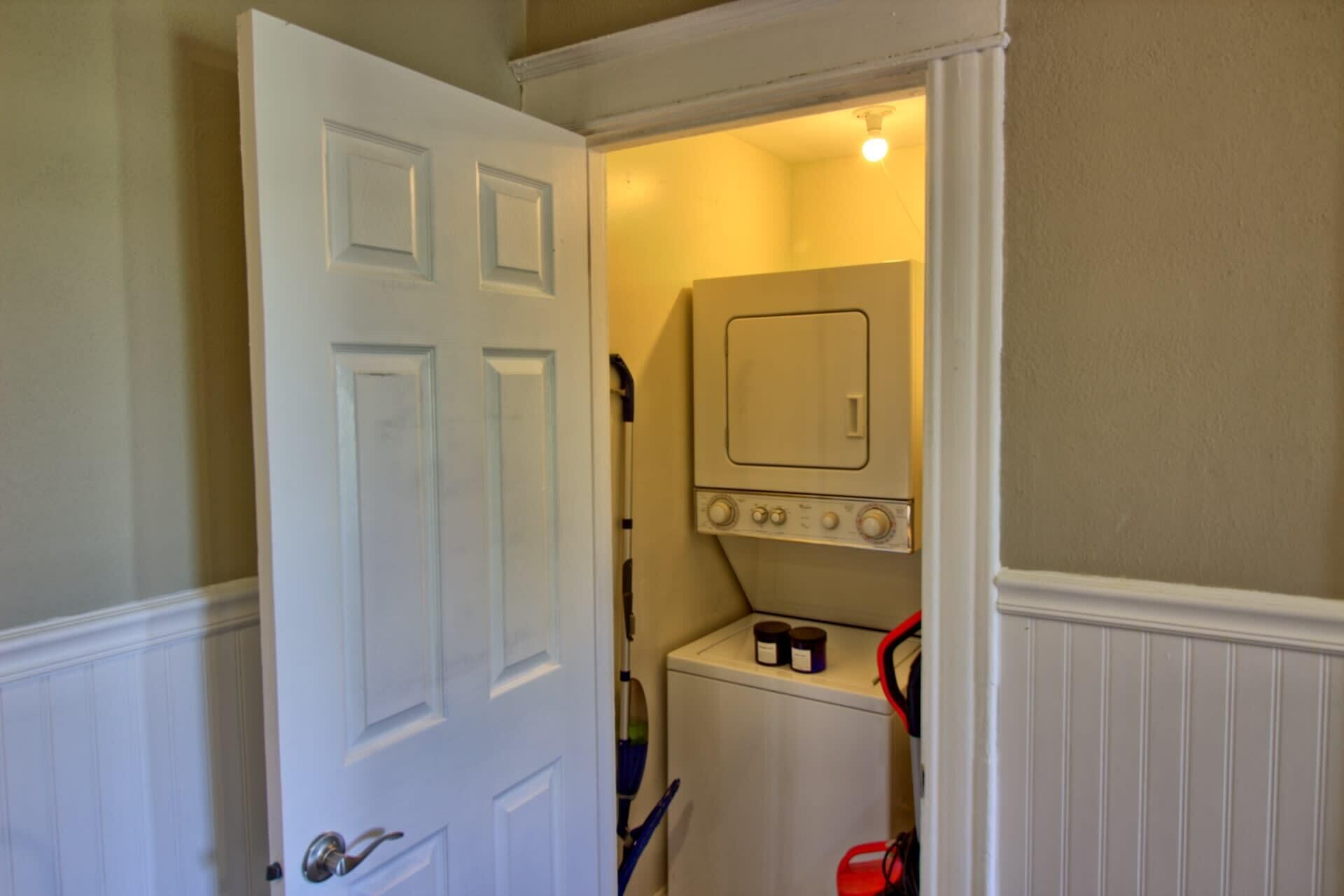 A laundry room with a washing machine, a drying rack, and a door leading to another room.