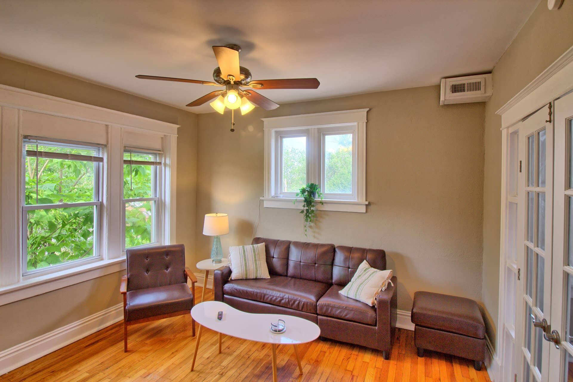 A living room with a brown leather sofa, a white coffee table, a brown leather armchair, and a ceiling fan.