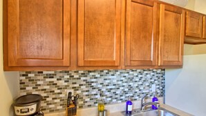 A kitchen with wooden cabinets, a coffee maker, a knife block, a bottle of olive oil, a bottle of blue dish soap, and a stainless steel sink. - Magnolia at TG Park | Free PK+WD+Pet Friendly (Saint Louis)