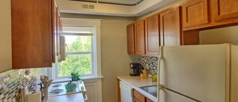 Une cuisine avec des meubles en bois, un réfrigérateur blanc, une cuisinière et une fenêtre donnant sur les arbres.