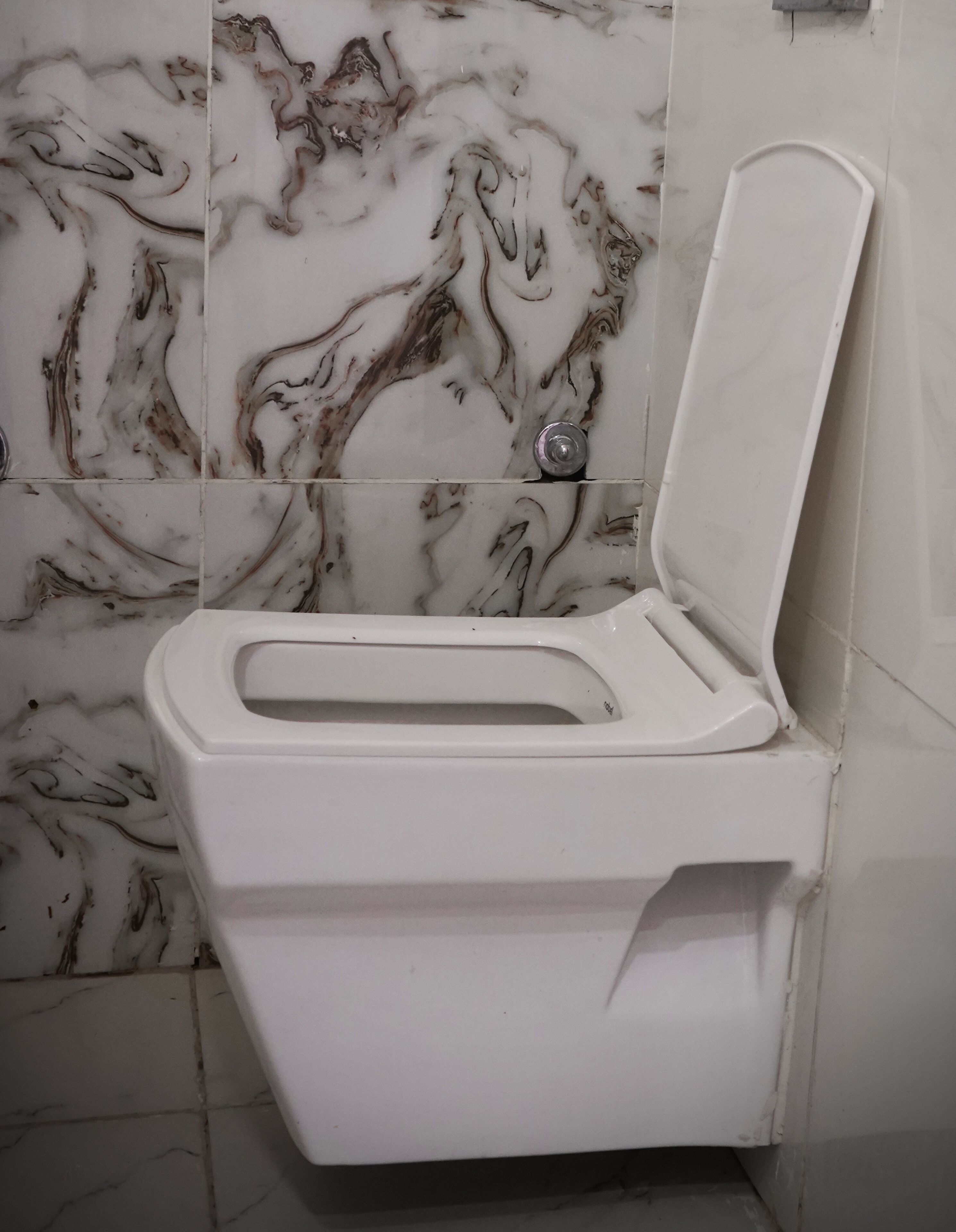 Eine weiße Toilette mit geschlossenem Deckel und einem Wand-Spülknopf.