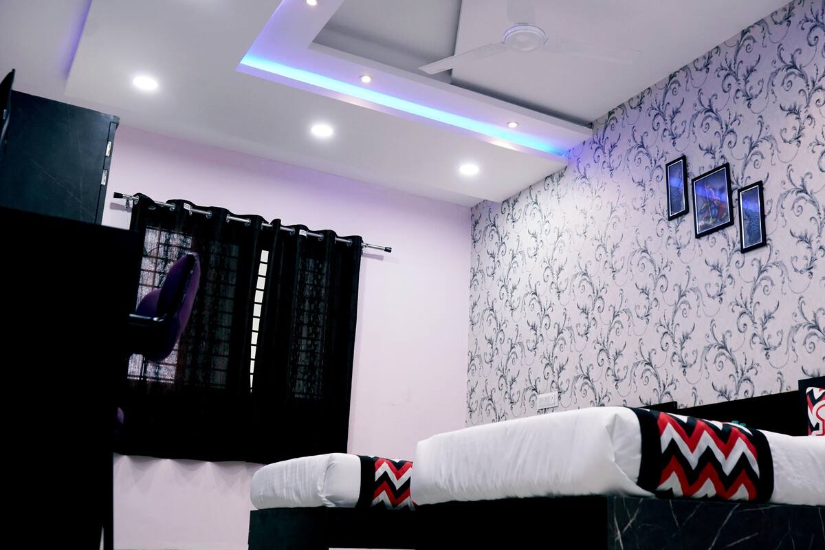 Una camera d'albergo con un letto, una finestra con tende e luci a soffitto, oltre a una parete con carta da parati decorata.
