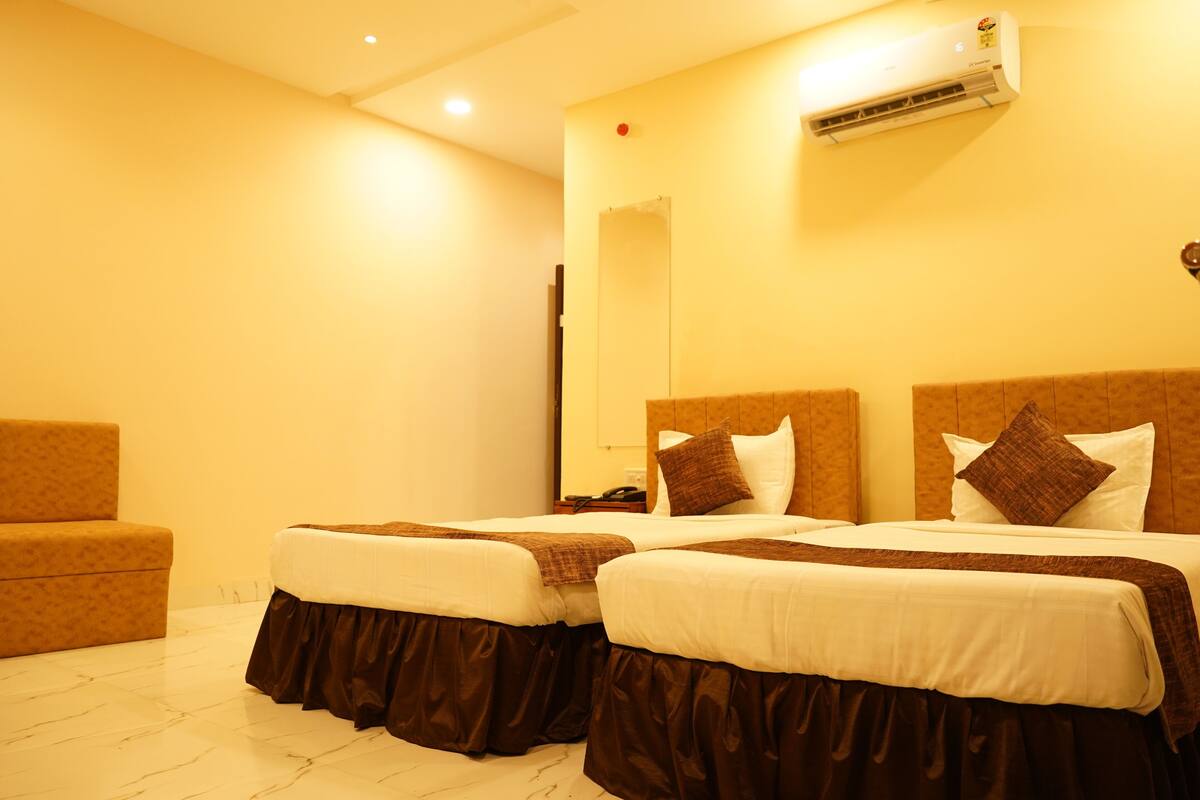 Habitación de hotel con dos camas, un sofá y un equipo de aire acondicionado en la pared.