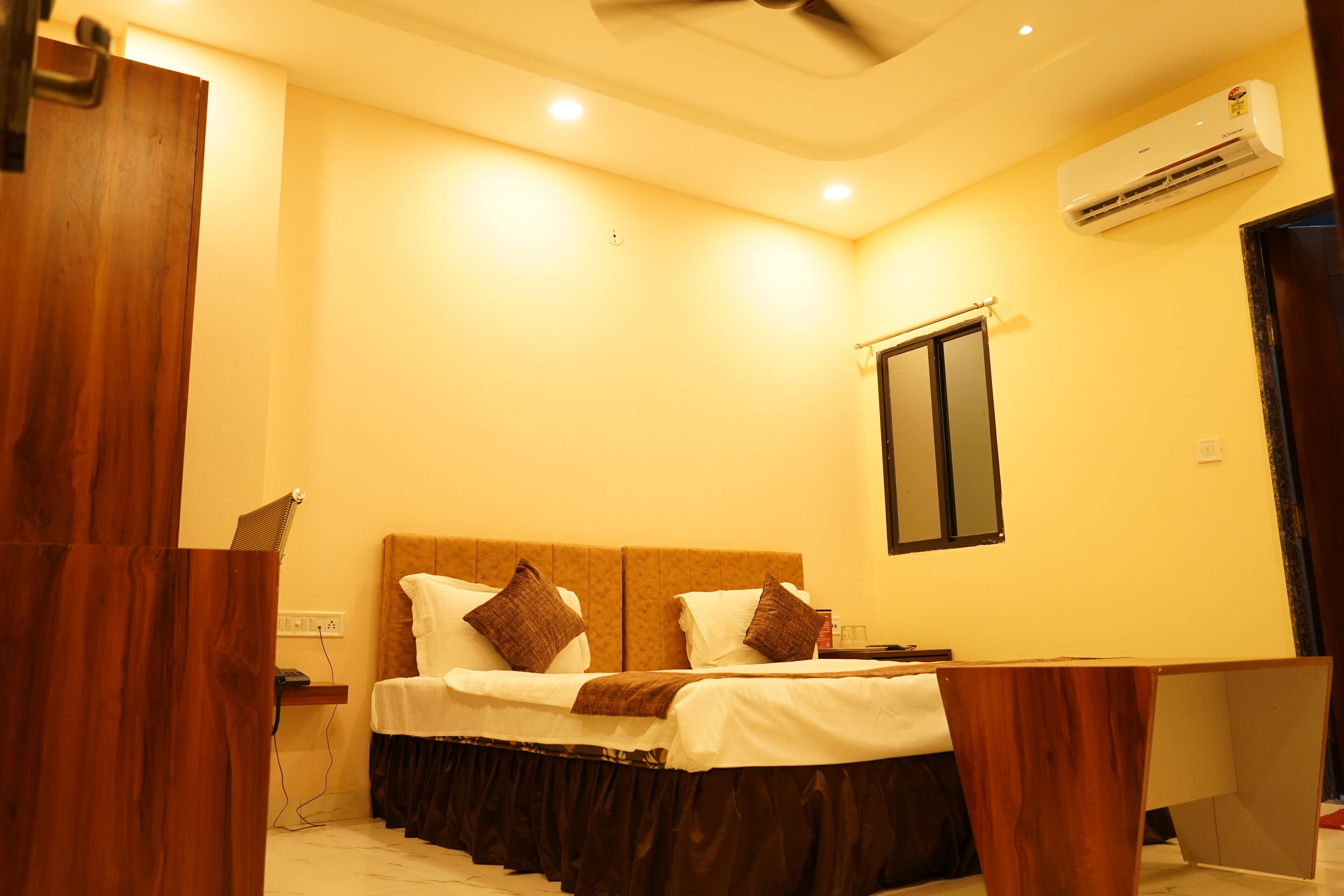 Una habitación de hotel con cama, mesita de noche y unidad de aire acondicionado.
