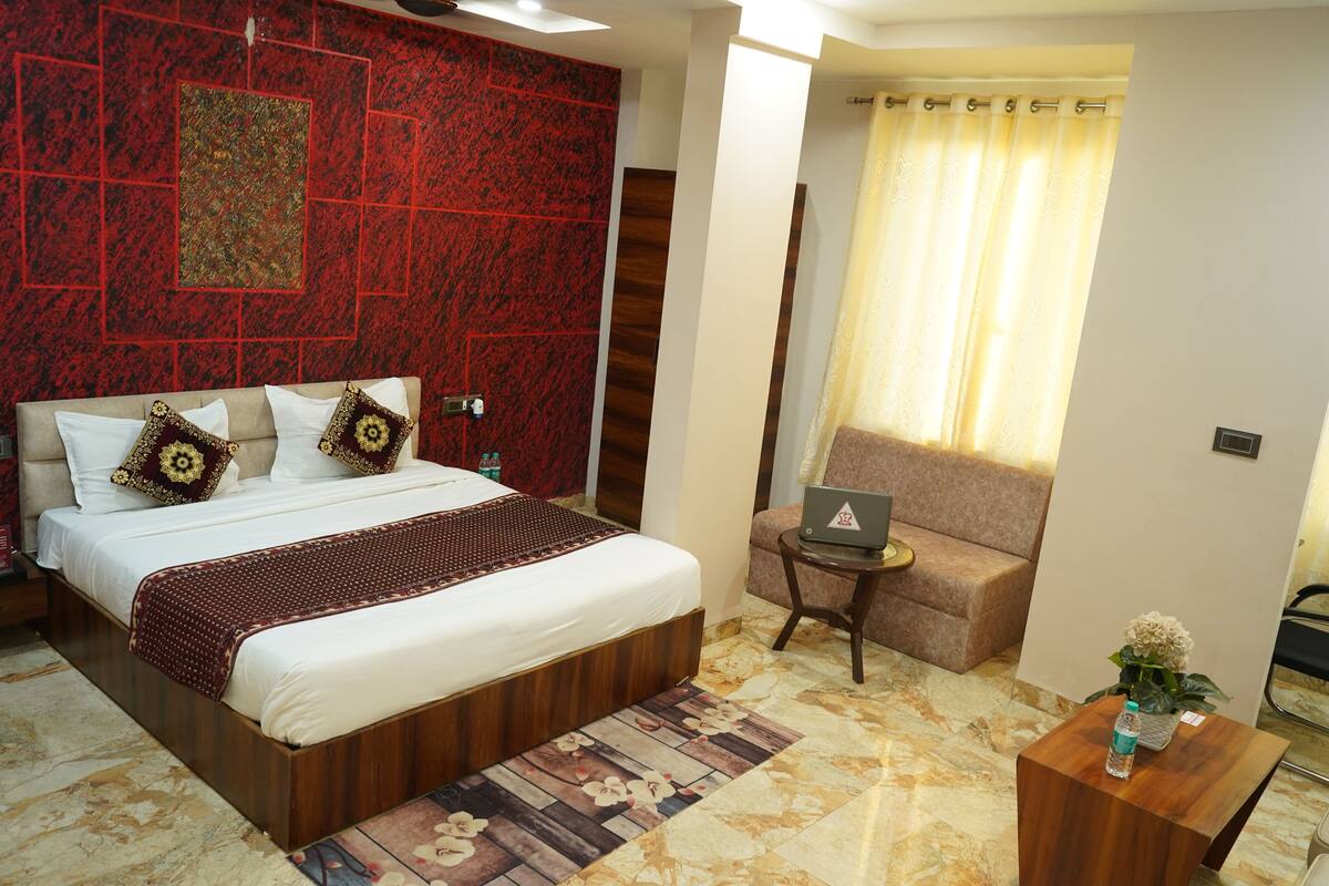 Habitación de hotel con una cama grande, un ordenador portátil sobre una mesita pequeña, un sofá y una alfombra decorativa.