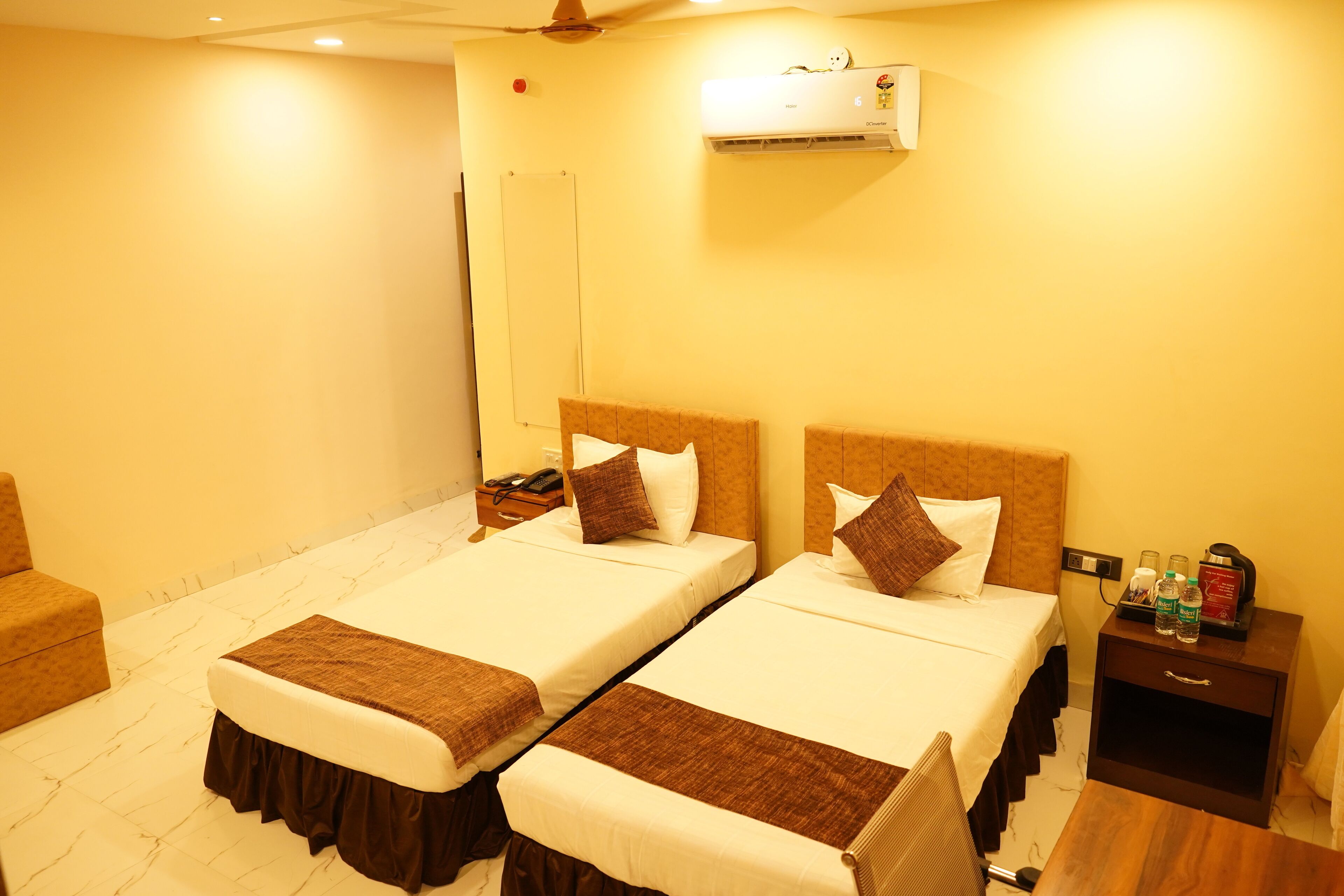 Een hotelkamer met twee bedden, een nachtkastje met toiletartikelen en een airconditioning aan de muur.