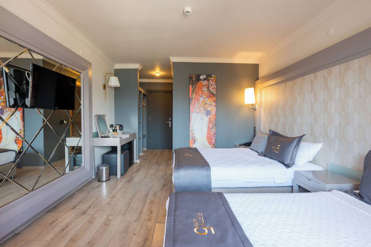 A hotel room with two beds, a desk, a TV, and a bathroom.