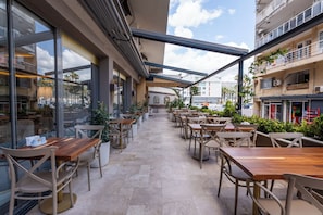 An outdoor cafe area with tables and chairs, large windows, and potted plants. - FİFTY5 SUİTE OTEL (Marmaris)