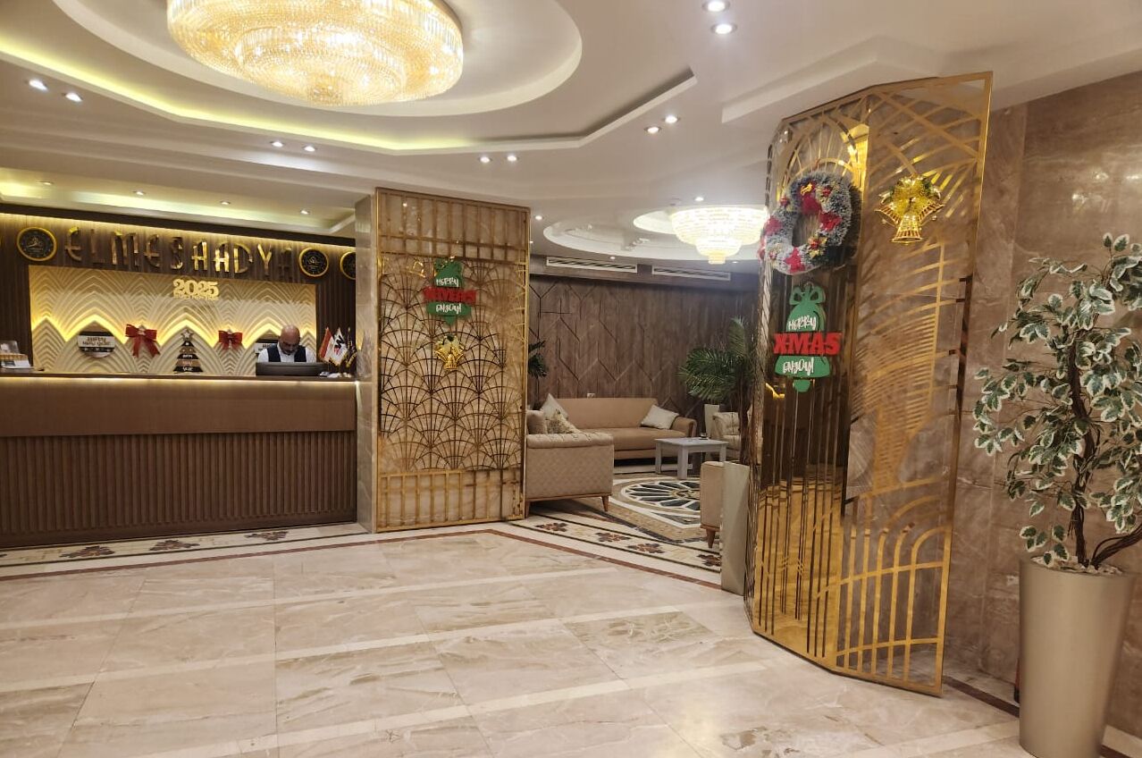 A hotel reception area with a modern design, featuring a reception desk, seating area, and decorative elements like wreaths and a large potted plant.