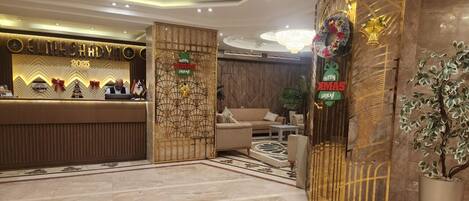 A hotel reception area with a modern design, featuring a reception desk, seating area, and decorative elements like wreaths and a large potted plant.