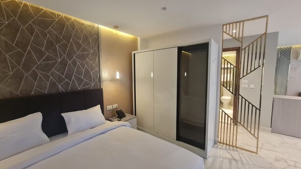 A modern hotel room with a large bed, a wardrobe, a desk with a phone, and a bathroom visible through a glass door. - el masaadya hotel  (Cairo)