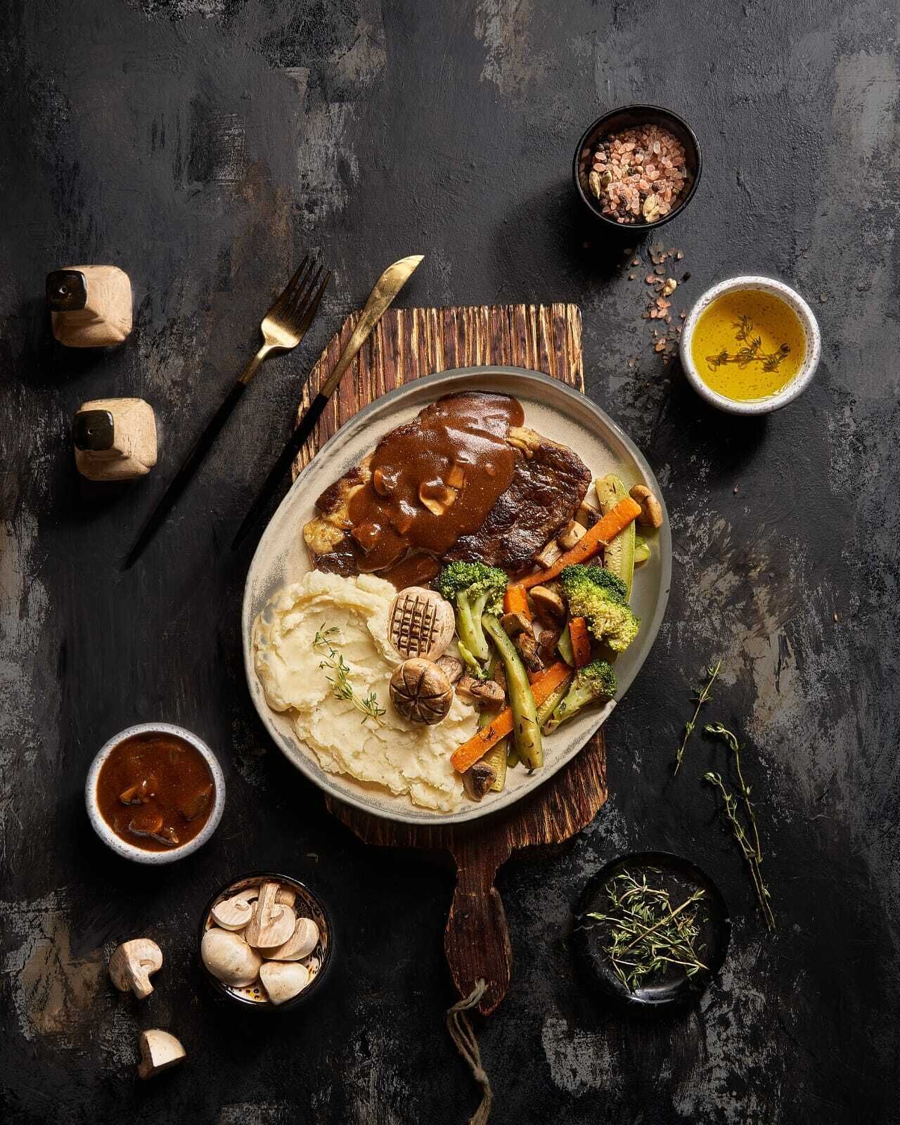 A plate of food with mashed potatoes, gravy, and vegetables on a dark surface.