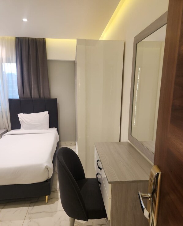 Una habitación de hotel con cama, escritorio con silla, un espejo grande y armario.