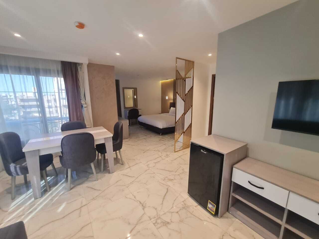 A hotel room with a dining table, chairs, a bed, a TV, and a minibar.