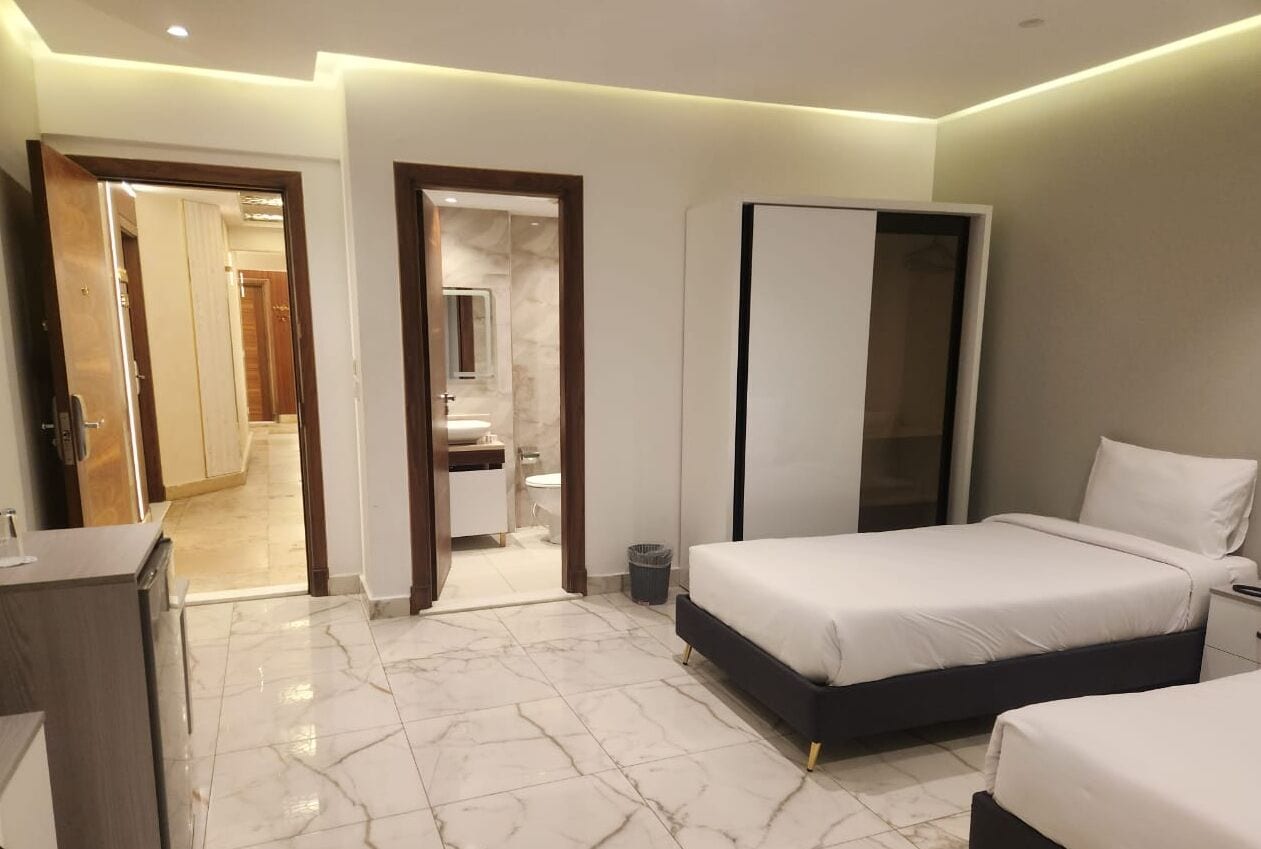 A modern hotel room with a marble floor, a large bed, a bedside table, and a wardrobe.