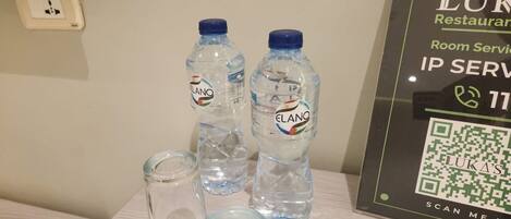 Una mesa con dos botellas de agua etiquetadas 'ELANO' y un vaso. Se ve un código QR y texto que indica 'Restaurante LUKA' y 'Servicio a la habitación' en la pared.