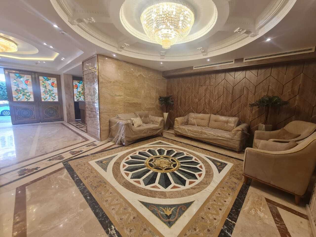 A luxurious lobby with a large, ornate circular carpet, plush seating, and a grand chandelier.